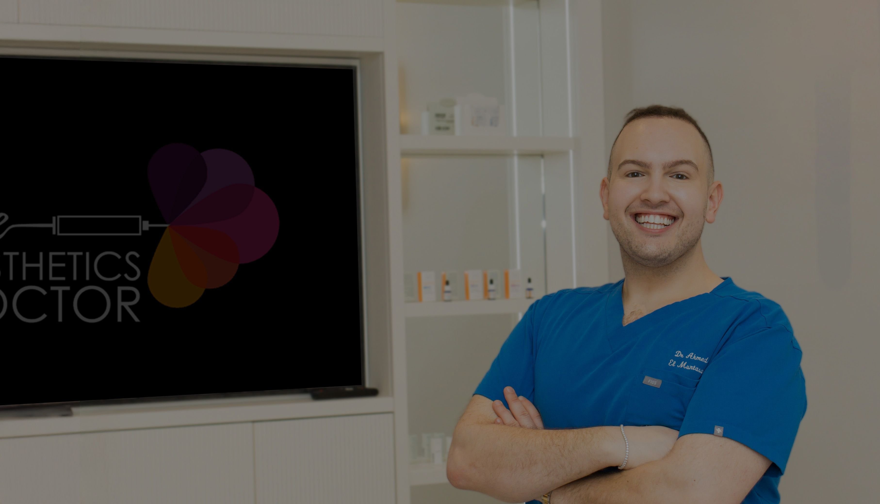 Dr Ahmed standing with arms crossed in The Aesthetics Doctor clinic, smiling at the camera